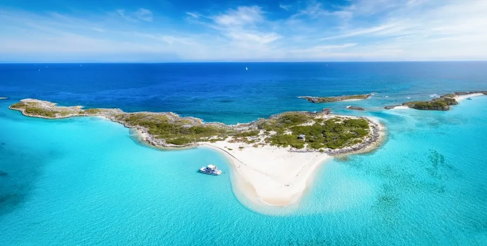 Aerial view of a pristine Caribbean island with white sand beaches, turquoise waters, and a boat anchored offshore.
