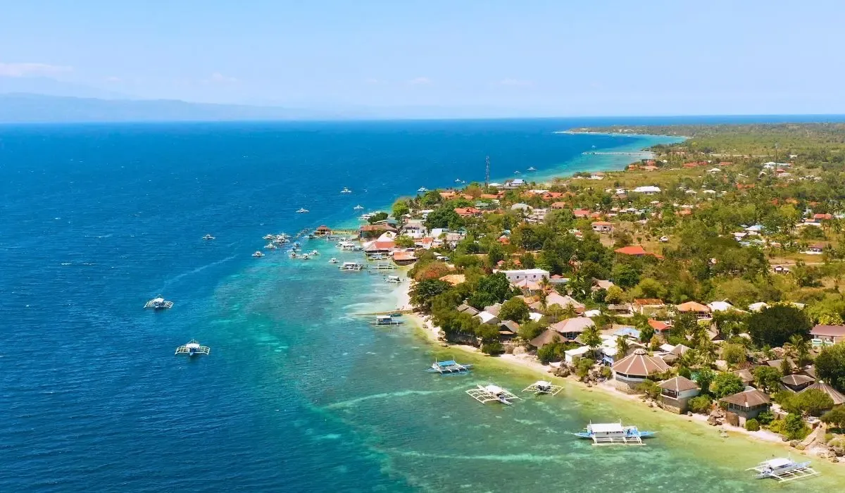 An aerial shot of Cebu City, highlighting a mix of modern buildings, historic churches, and the surrounding sea with boats dotting the harbor.​