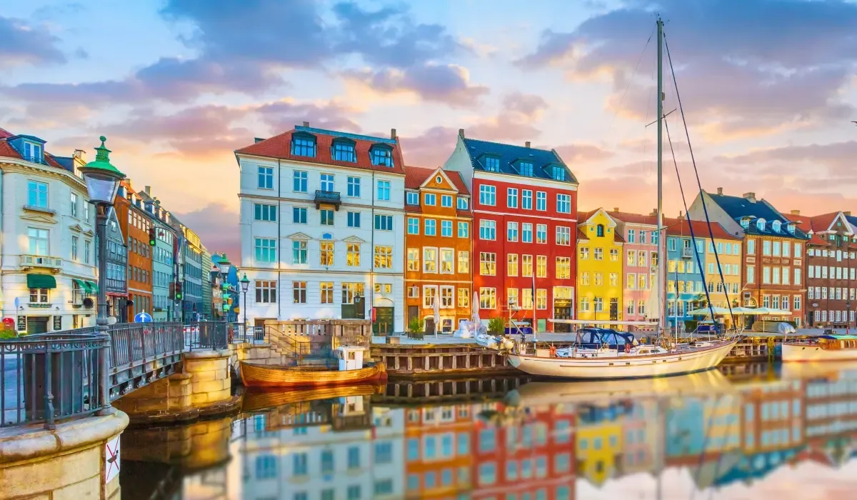 Colorful historic buildings and boats along the Nyhavn canal in Copenhagen, Denmark, under a vibrant sunset sky. Canadians considering buying property in Denmark can benefit from competitive CAD to DKK exchange rates and secure money transfers for international real estate transactions.