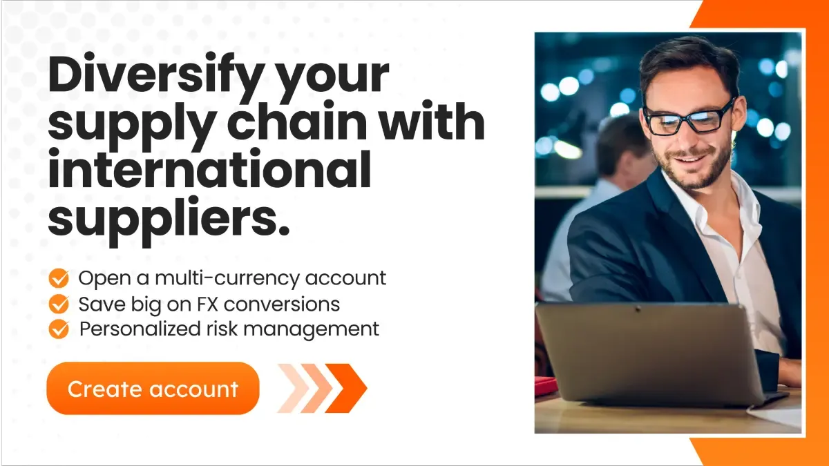 A smiling businessman wearing glasses and a suit is working on a laptop in a modern office with blurred colleagues in the background. The text overlay reads: "Diversify your supply chain with international suppliers." Below, bullet points highlight benefits like opening a multi-currency account, saving on FX conversions, and personalized risk management. A bright orange button says "Create account."