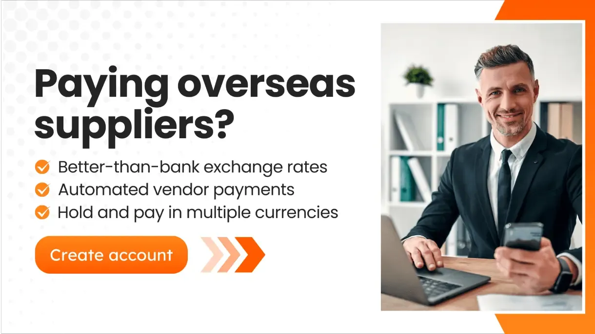 Professional man in a suit smiling while holding a phone at his desk, next to a call-to-action highlighting benefits of paying overseas suppliers in their local currency, including better exchange rates and multi-currency support.