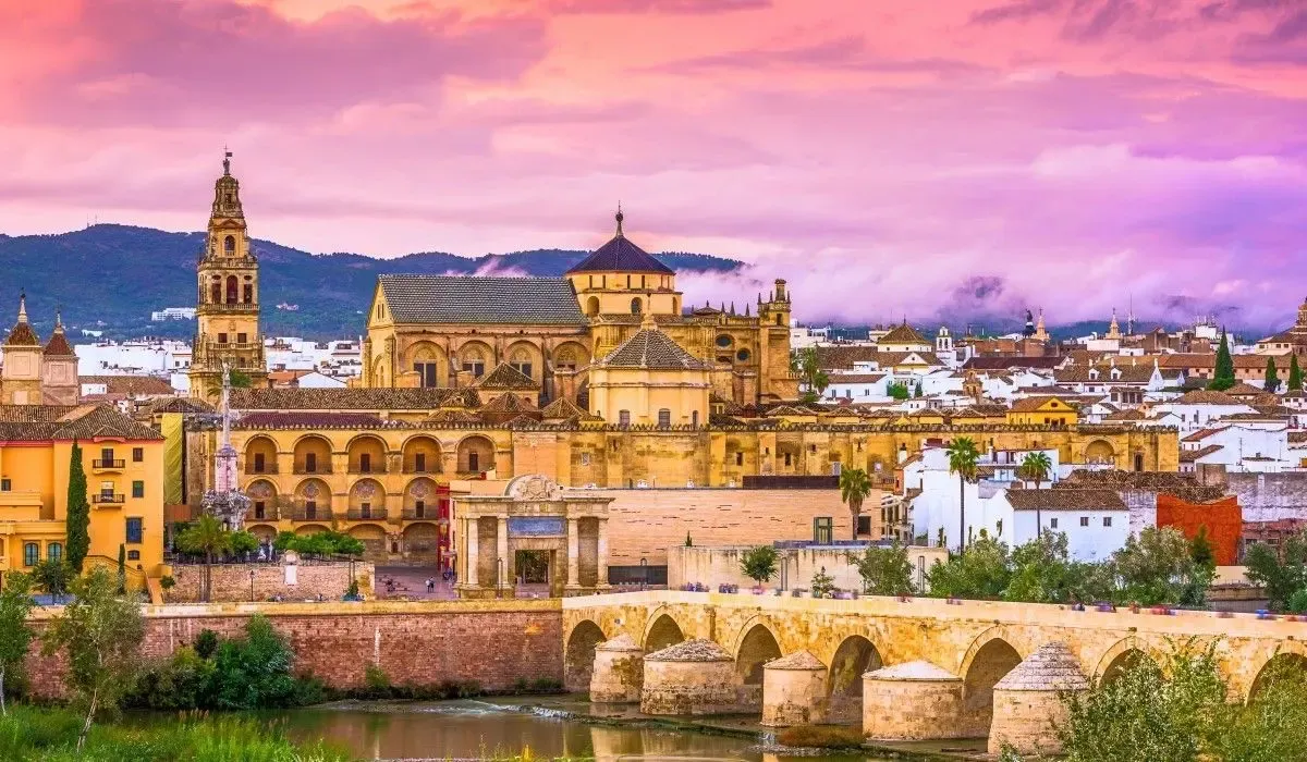 Historic skyline of Córdoba, Spain with the stunning Mosque–Cathedral and Roman Bridge at sunset under pink and purple skies. Canadians interested in buying property in Spain can take advantage of competitive CAD to EUR rates and low-cost transfers with MTFX.