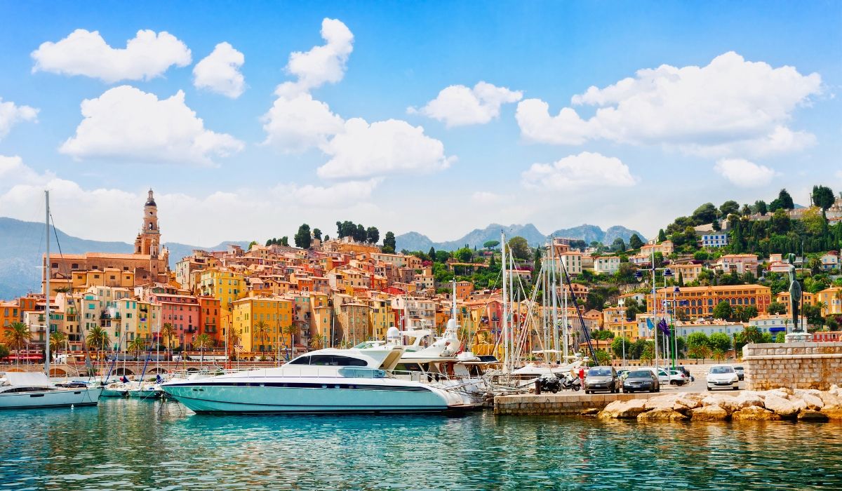 A stunning view of the Côte d'Azur coastline with azure waters, rocky cliffs, and luxurious yachts anchored near the shore.