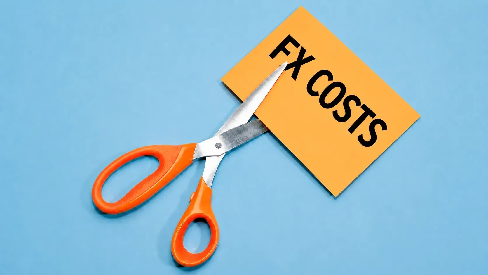 Orange-handled scissors cutting through a paper card labeled “FX COSTS” on a light blue background, symbolizing foreign exchange cost reduction.