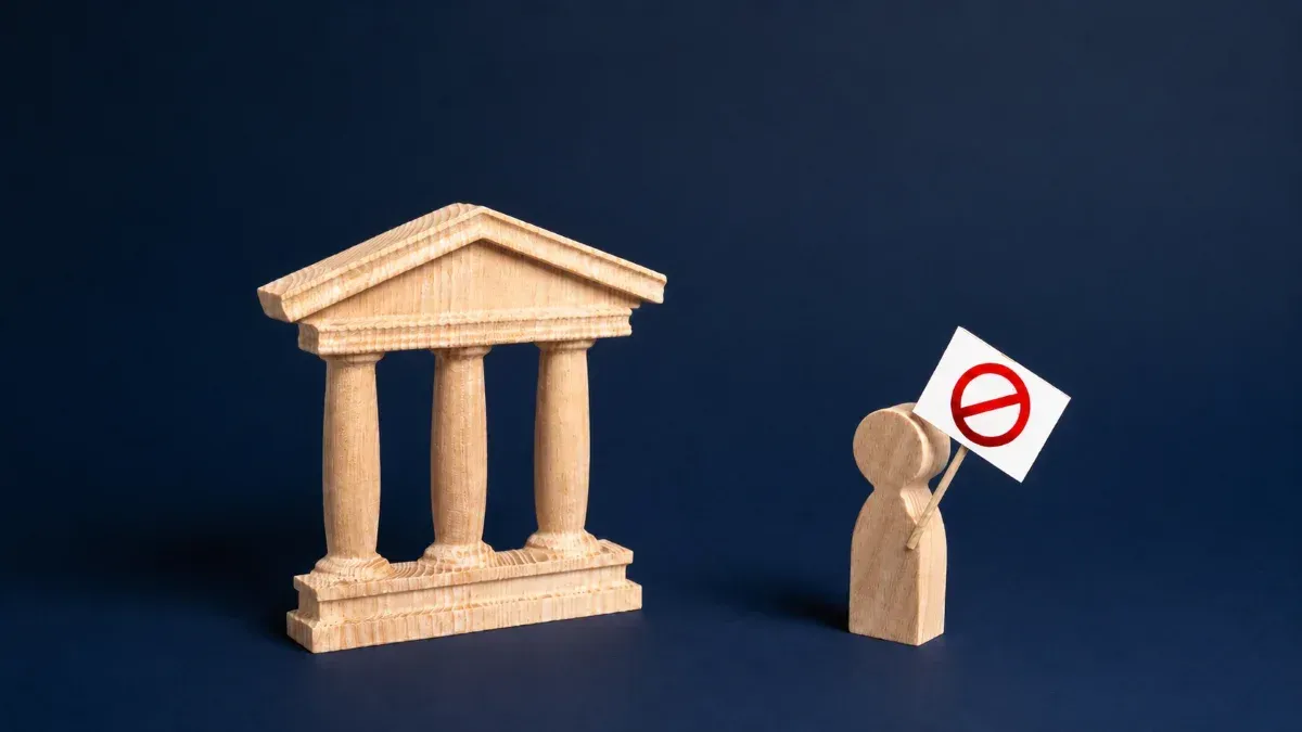 Wooden bank model with a person holding a no-entry sign, representing Canadians choosing alternatives to bank transfers for sending money abroad.