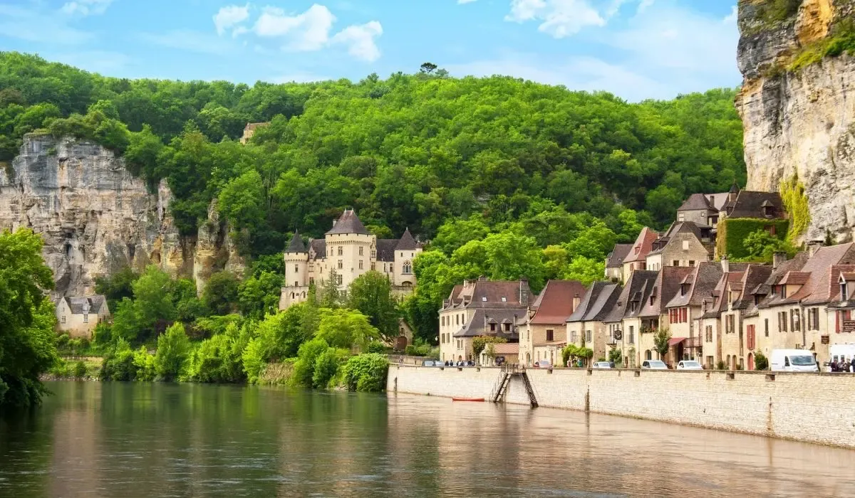 Historic riverside village in Dordogne, France with medieval stone houses and a castle nestled against green cliffs. Canadians buying property in France can benefit from competitive CAD to EUR rates and cost-effective transfers with MTFX.