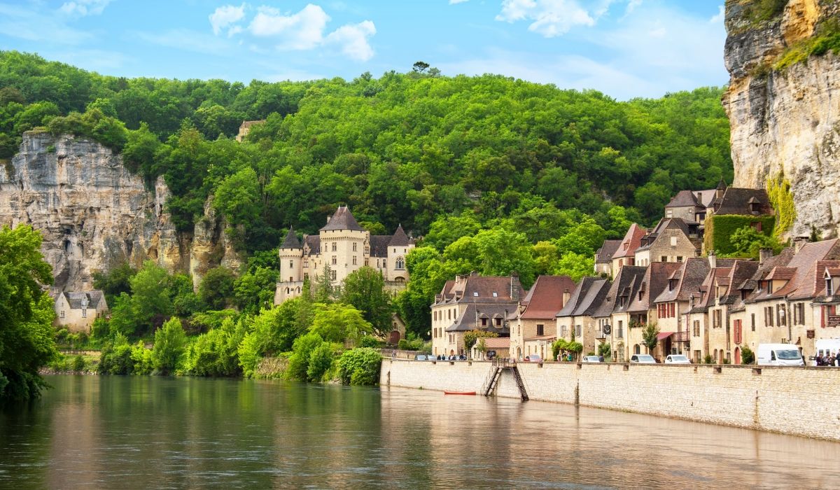 A tranquil countryside image of Dordogne, showcasing a historic stone farmhouse surrounded by lush greenery and rolling hills.