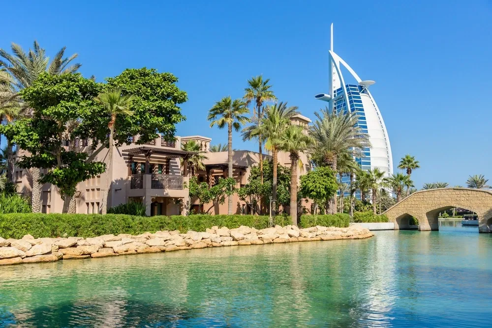 Scenic view of the Burj Al Arab hotel and traditional style villas surrounded by lush greenery and water canals at Madinat Jumeirah.