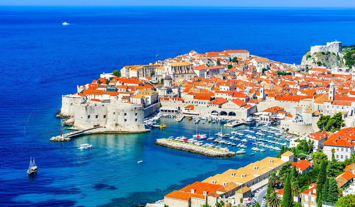 Aerial view of the historic walled city of Dubrovnik with its terracotta rooftops and marina set against the deep blue Adriatic Sea.