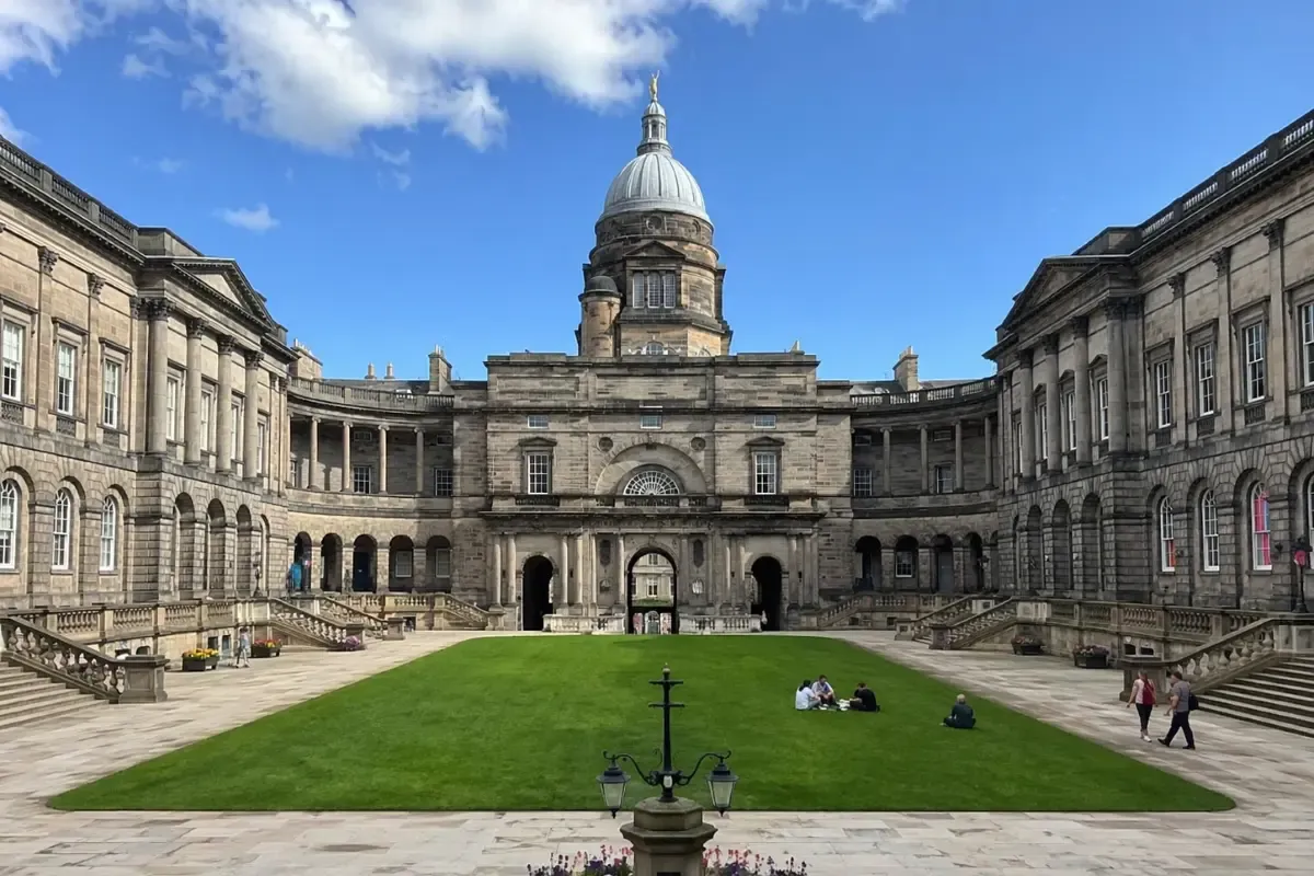 University of Edinburgh courtyard featuring classical stone buildings, a central lawn, domed tower, and students relaxing in the open campus square.
