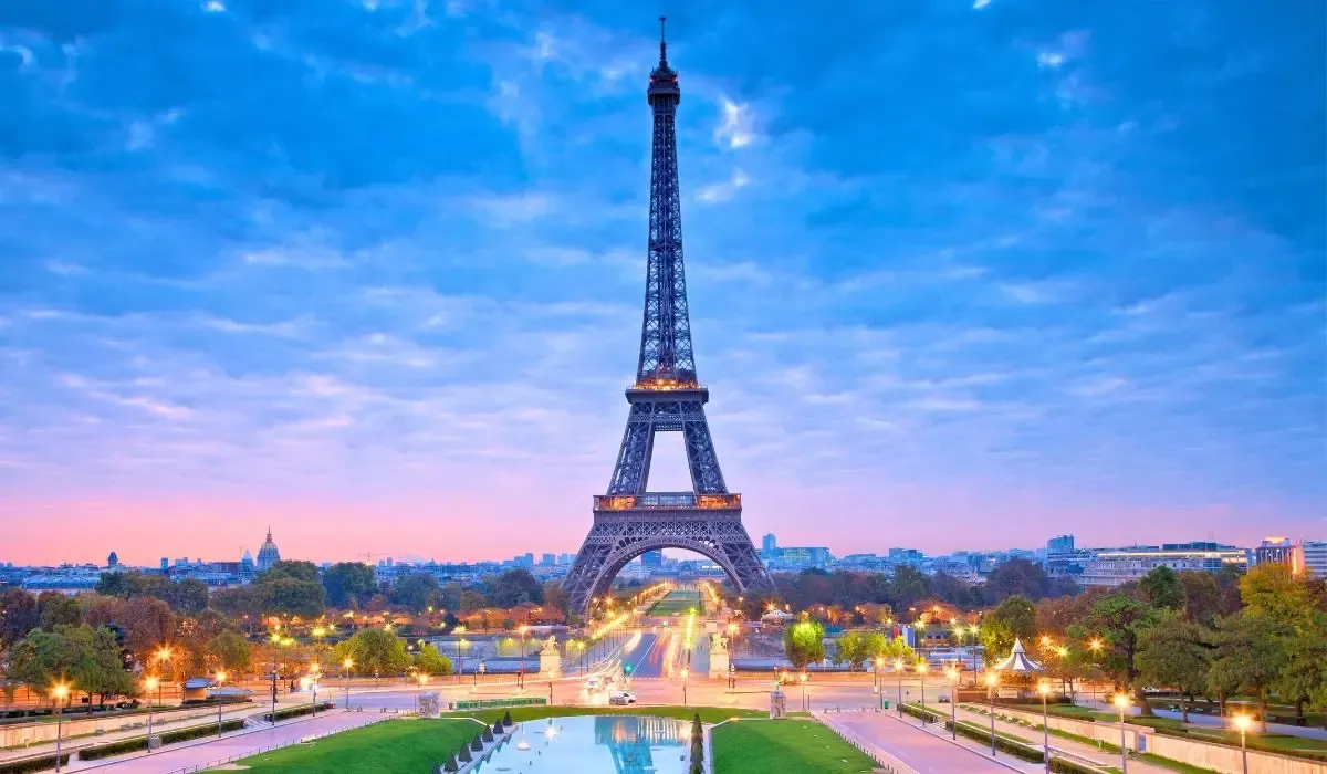 A view of Paris, France, featuring the Eiffel Tower rising above the city's rooftops, with the Seine River and historic bridges in the foreground.