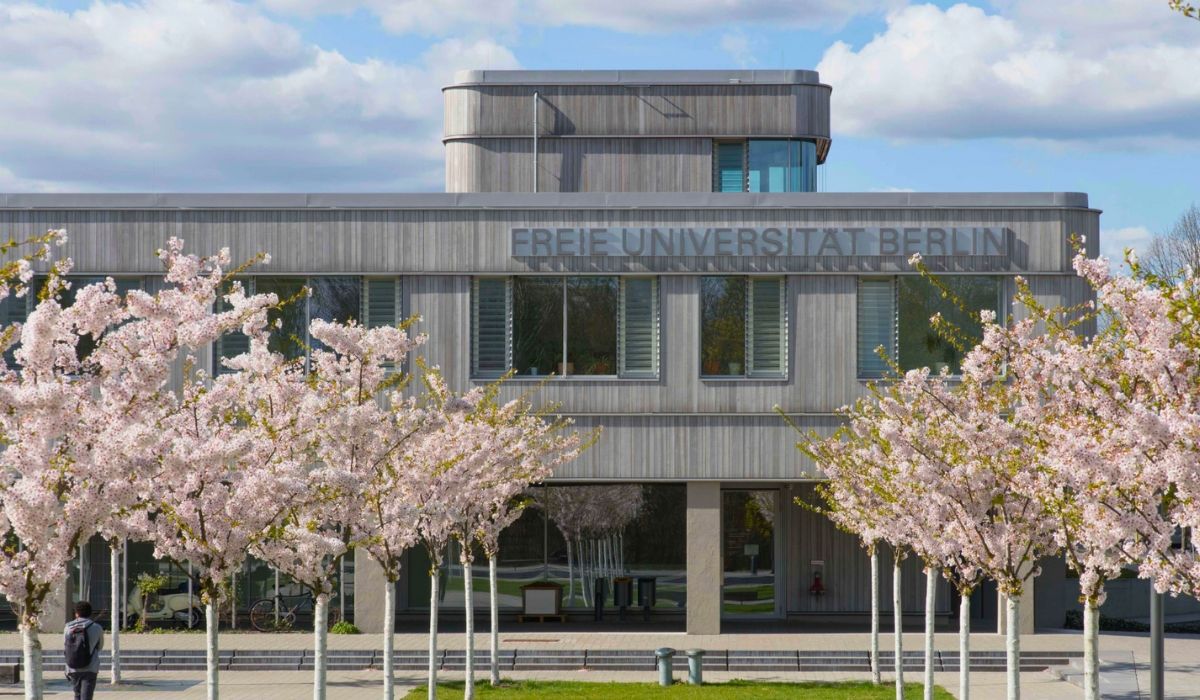 Exterior of the Free University of Berlin, featuring a minimalist modern building with “FREIE UNIVERSITÄT BERLIN” signage and cherry blossom trees in bloom.