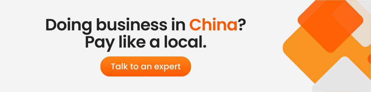 A banner ad with the text "Doing business in China? Pay like a local." The word "China" is highlighted in orange. Below, an orange button reads "Talk to an expert." The background features an abstract geometric design in shades of orange, white, and gray.