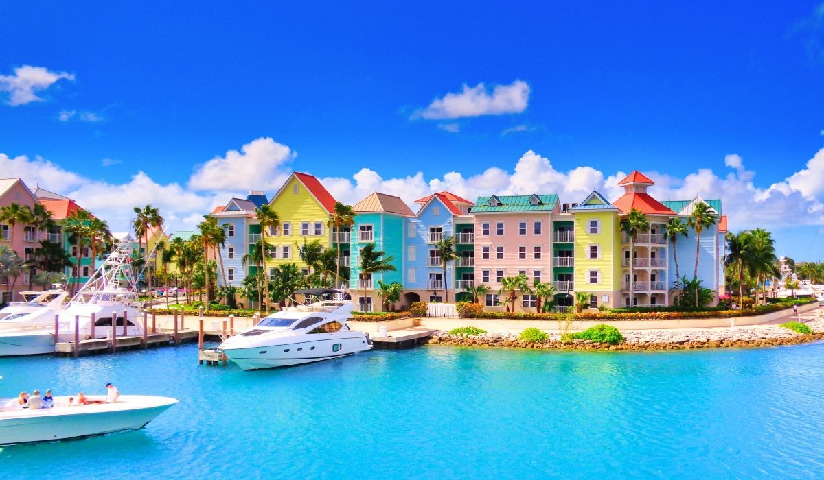 Colourful waterfront condos and yachts docked in a marina in the Bahamas under a clear blue sky.