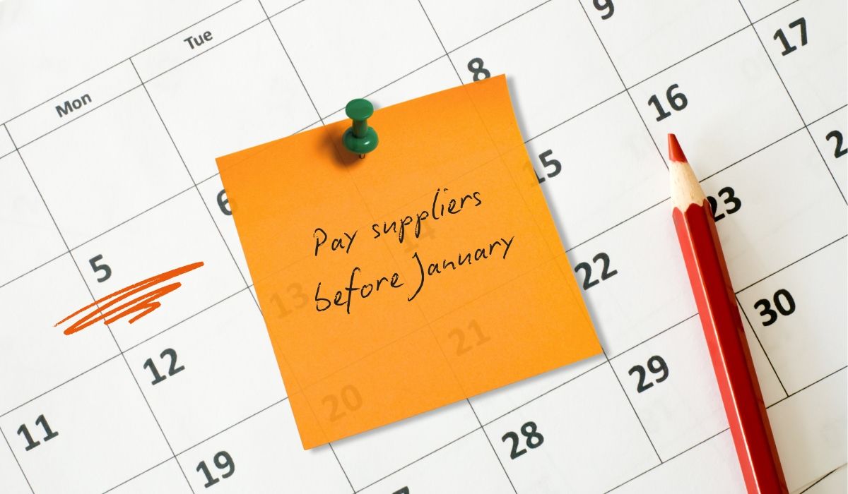 A closeup of a calendar page with sticky note on it saying "Pay suppliers before January"
