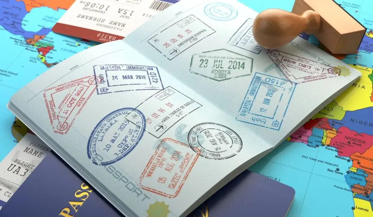 A passport with multiple stamps from various countries, including Malaysia, Colombia, and others. A boarding pass and a map are visible in the background.
