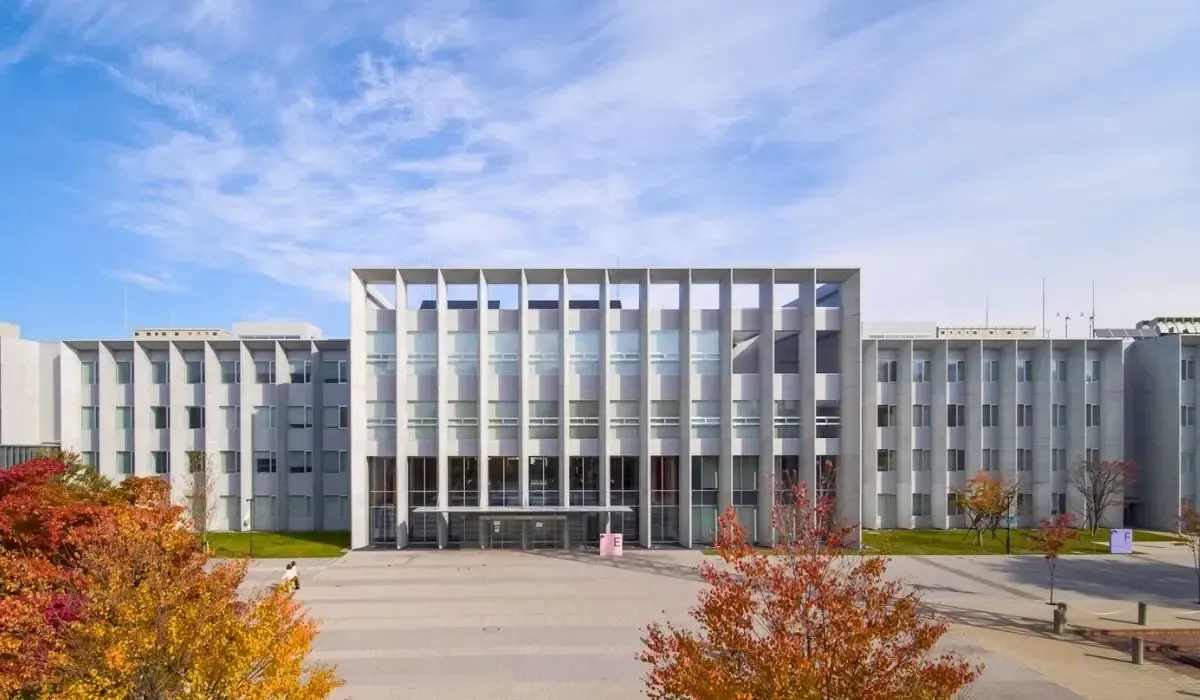 Hokkaido University modern campus building with a white geometric facade, large windows, and autumn trees in the foreground.