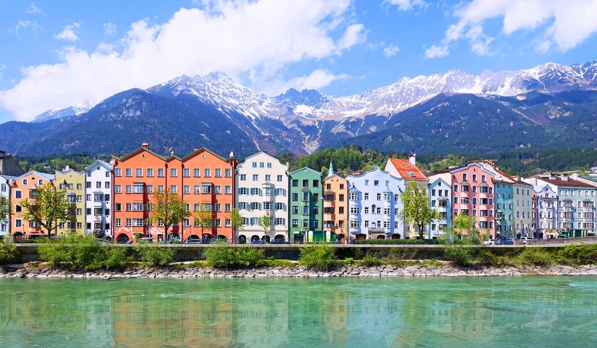 A picturesque view of Innsbruck’s colorful buildings along the Inn River, set against the dramatic backdrop of the Austrian Alps.