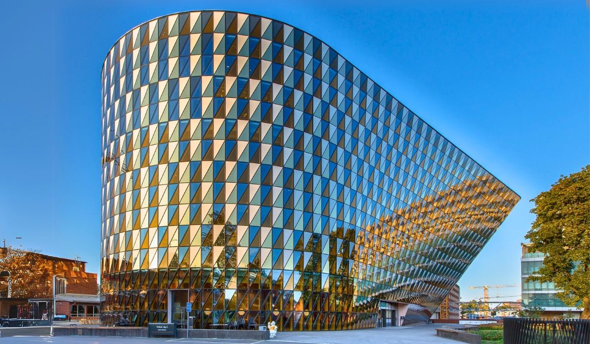 Modern glass façade of the Karolinska Institute in Stockholm, Sweden, reflecting sunlight against a clear blue sky.