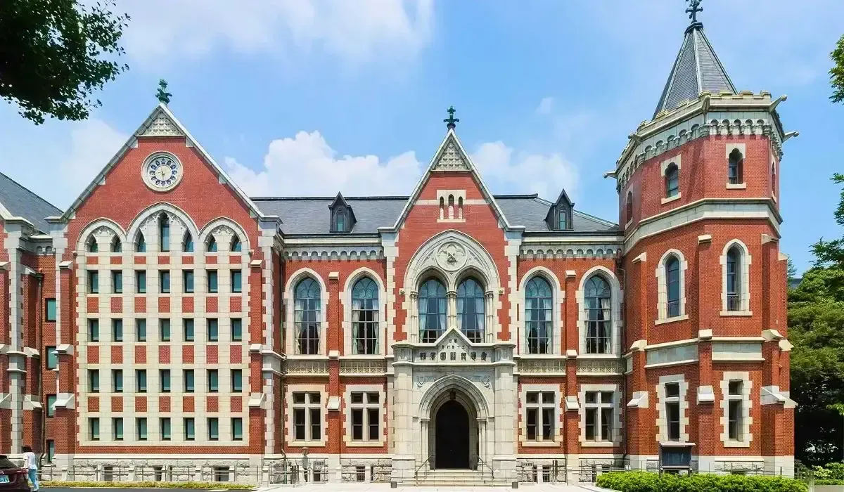 Keio University’s red-brick historic campus building with Gothic-style arched windows, a clock, and a corner tower under a blue sky.