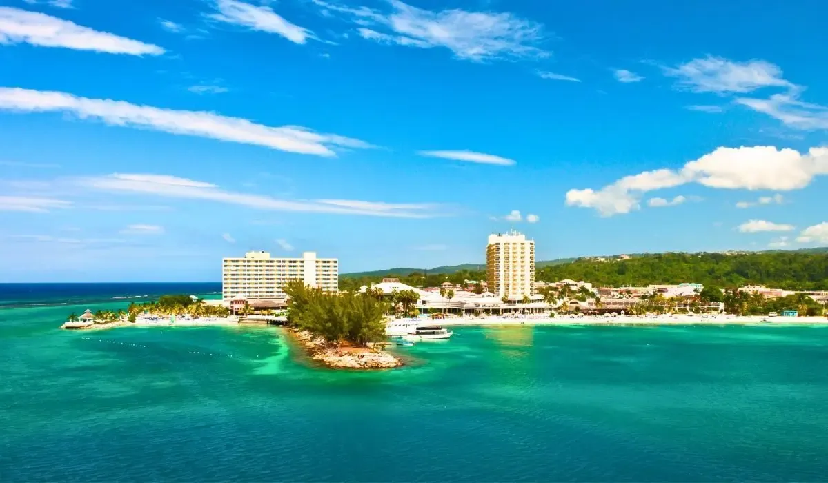 Coastal scene of Kingston, Jamaica, featuring beachfront hotels, turquoise sea, and lush tropical surroundings under sunny skies. Canadians purchasing property in Jamaica can optimize their CAD to USD conversions and reduce transfer costs with MTFX.