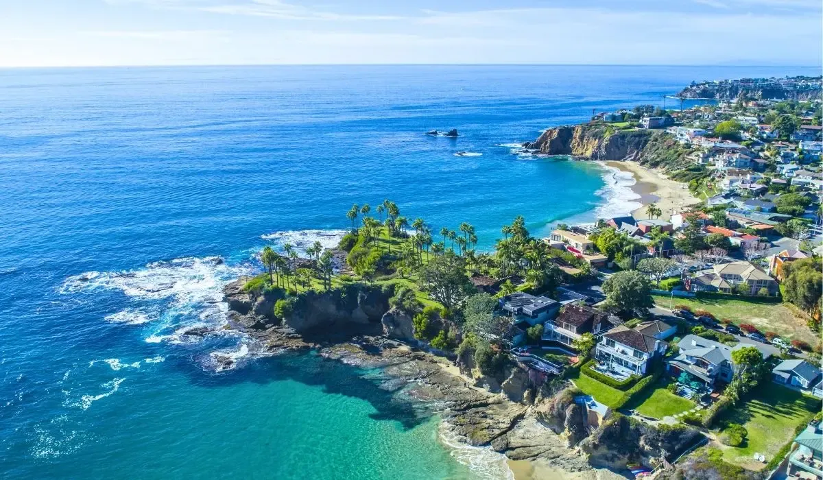 A scenic view of Laguna Beach's coastline, featuring sandy shores, rocky cliffs, and the Pacific Ocean under a clear blue sky.