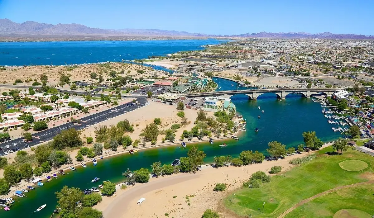 A scenic image of Lake Havasu with calm blue waters, the London Bridge, and surrounding desert hills under a sunny sky.