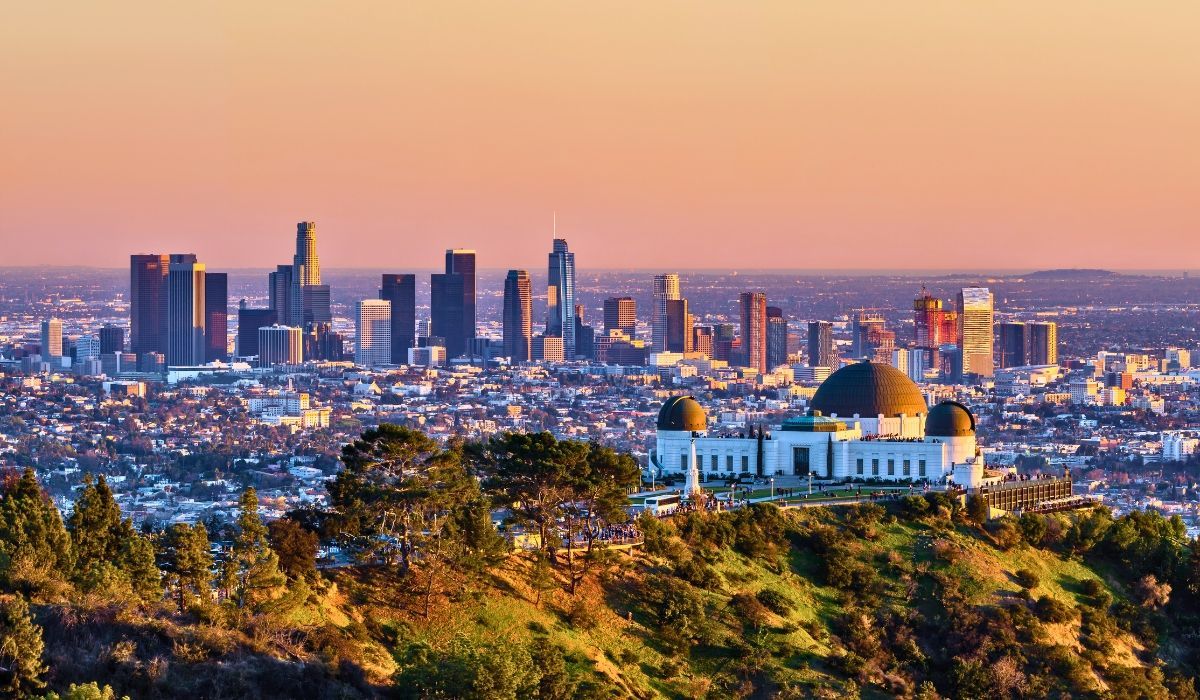 A panoramic view of downtown Los Angeles, showcasing modern skyscrapers with the San Gabriel Mountains in the background.