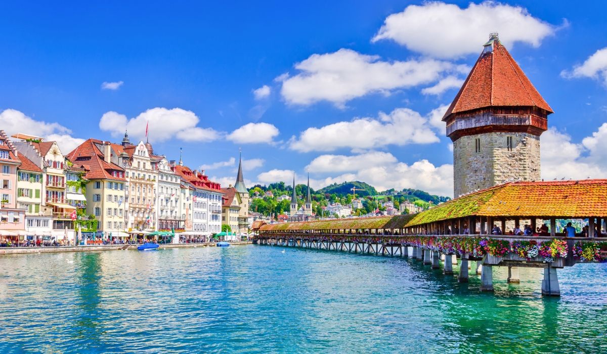 Scenic view of Chapel Bridge and the Water Tower in Lucerne, Switzerland, surrounded by colorful historic buildings and a vibrant lakefront.
