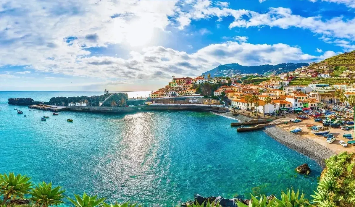 A sunny harbor view in Madeira, Portugal, with turquoise waters, fishing boats, and hillside homes, representing the transactional aspect of transferring funds internationally and converting CAD to EUR for property investments in Portugal’s island regions.