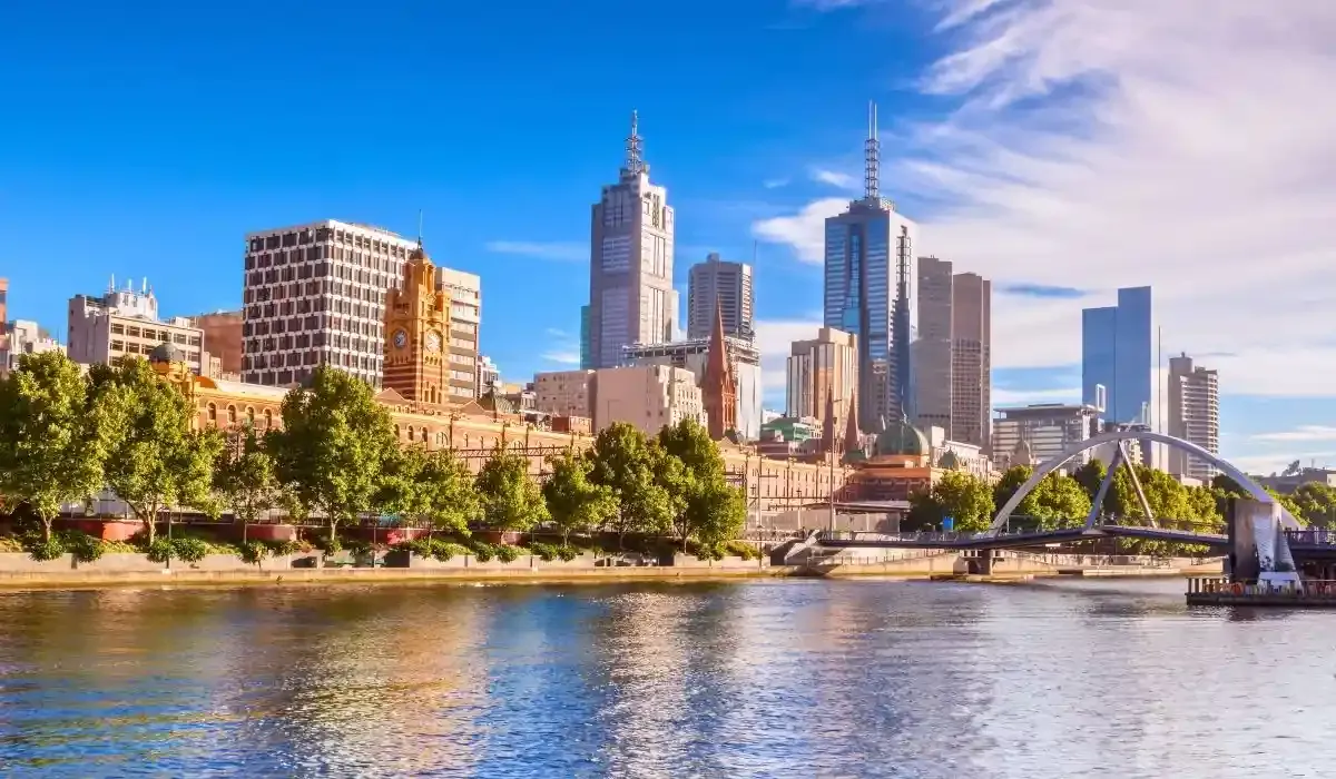 Cityscape of Melbourne with historic Flinders Street Station and modern skyscrapers lining the Yarra River.