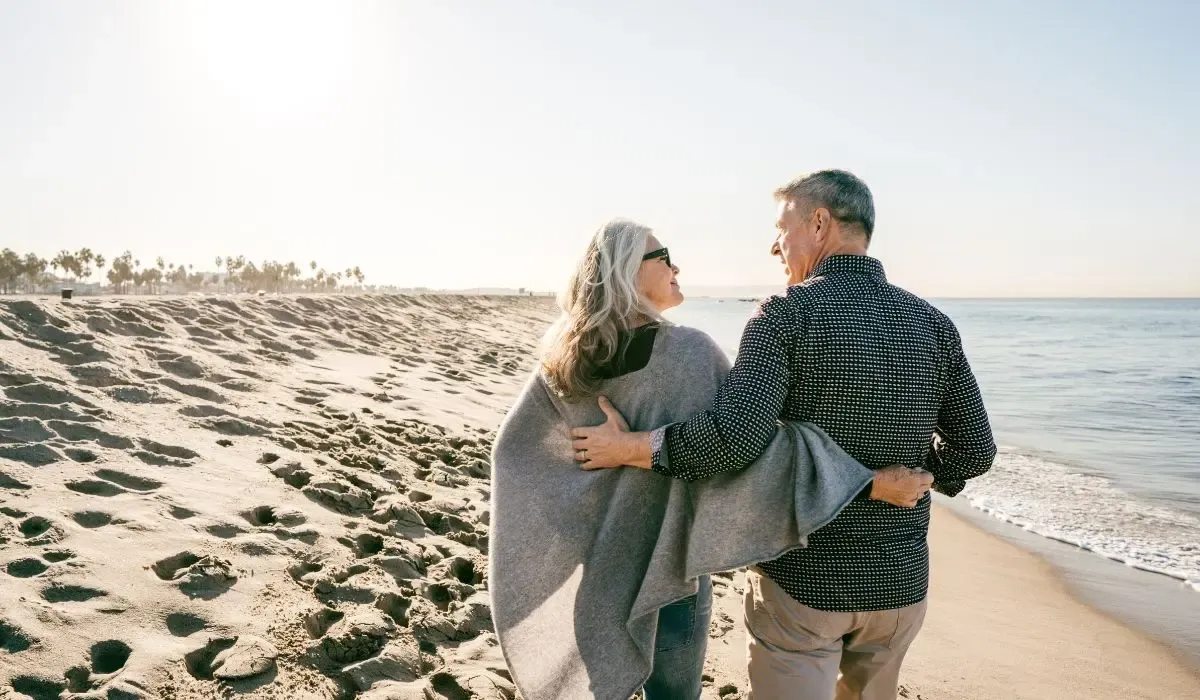 Retired couple walking along a sunny beach, representing Canadian snowbirds relocating for winter