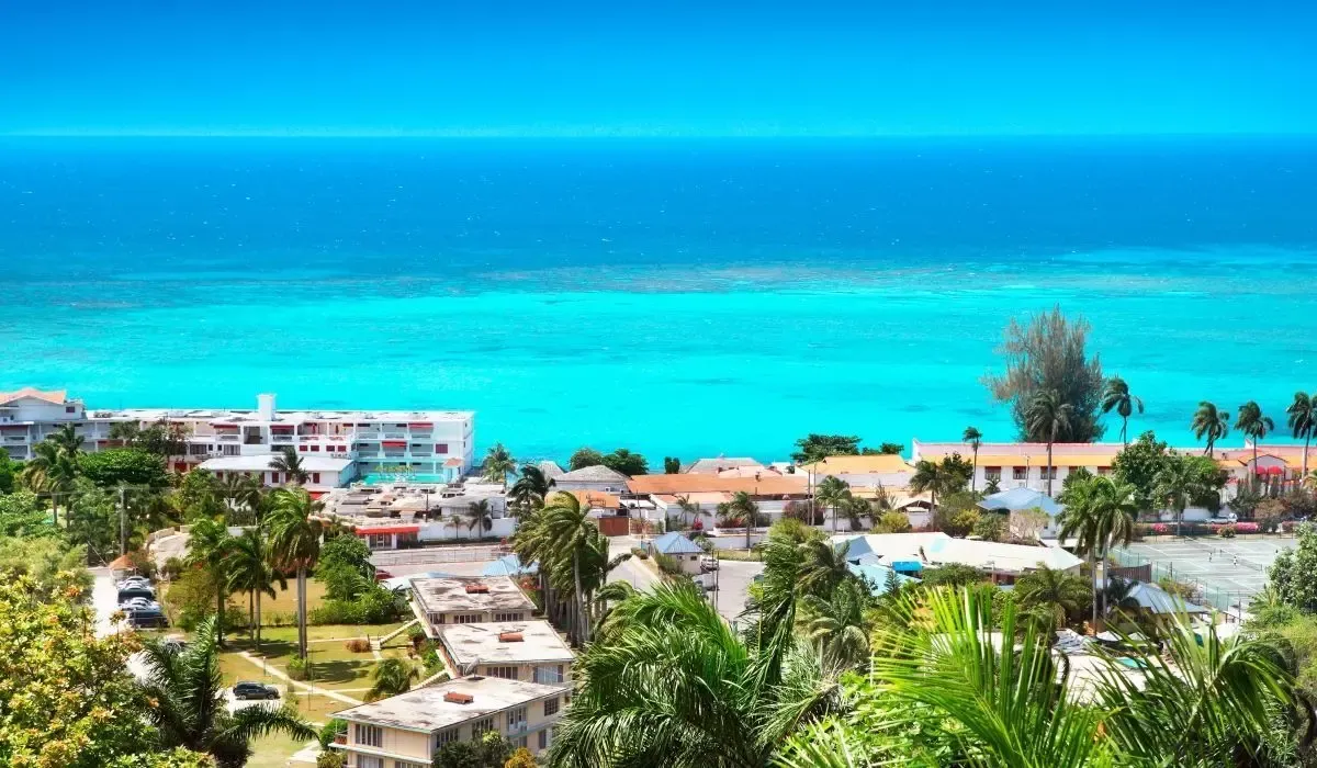 Montego Bay skyline in Jamaica with vibrant turquoise ocean waters, beachfront resorts, palm trees, and clear blue skies. Canadians investing in property in Jamaica can secure competitive CAD to USD exchange rates and low-fee money transfers through MTFX.