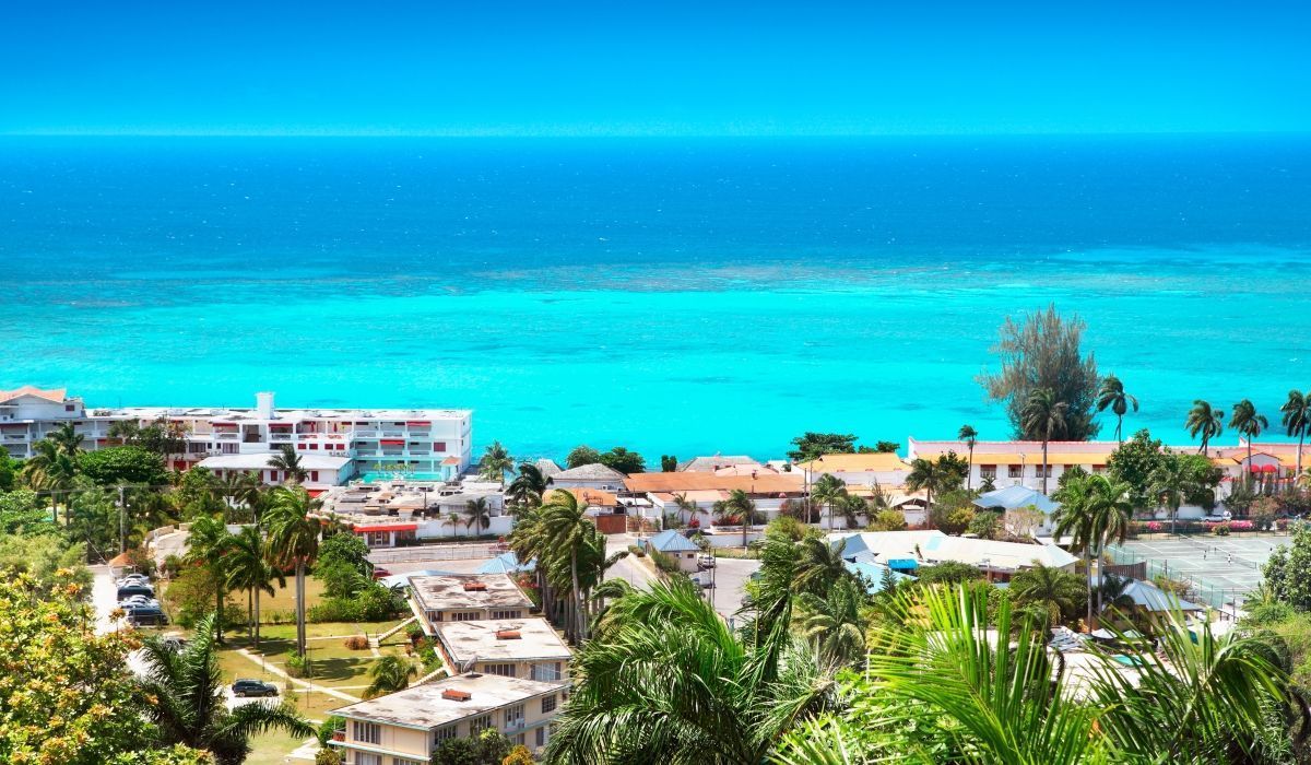 Aerial view of Montego Bay, Jamaica, showing coastal buildings, palm trees, and the bright turquoise waters of the Caribbean Sea.