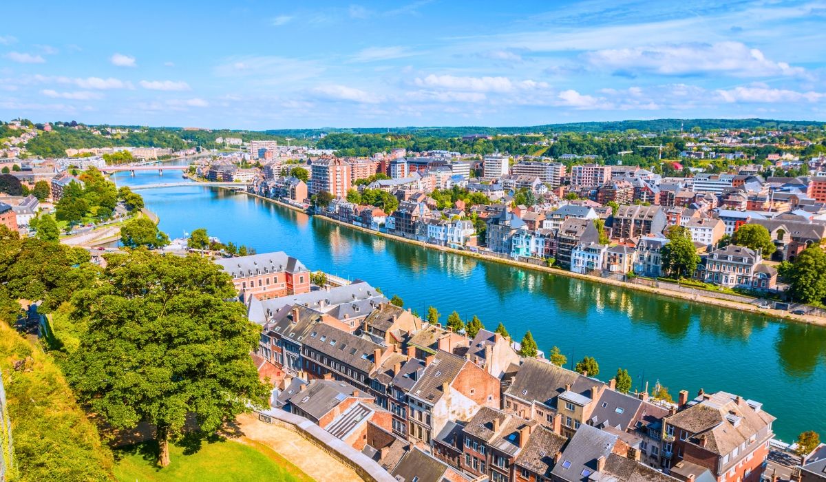 Scenic aerial view of the Meuse River running through Namur, Belgium, surrounded by colorful houses and green landscapes.