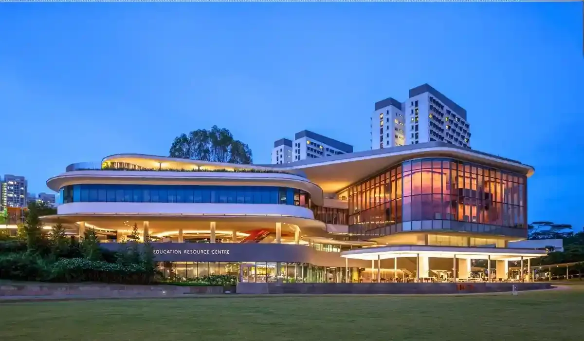 Modern architecture of the National University of Singapore campus at dusk, with illuminated glass facades and high-rise buildings in the background.