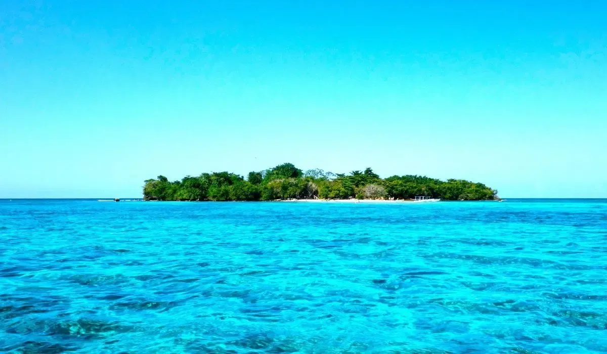 Negril, Jamaica, featuring a lush tropical island surrounded by brilliant turquoise waters under a clear blue sky. Canadians buying property in Jamaica can access favourable CAD to USD exchange rates and low-cost international transfers with MTFX.