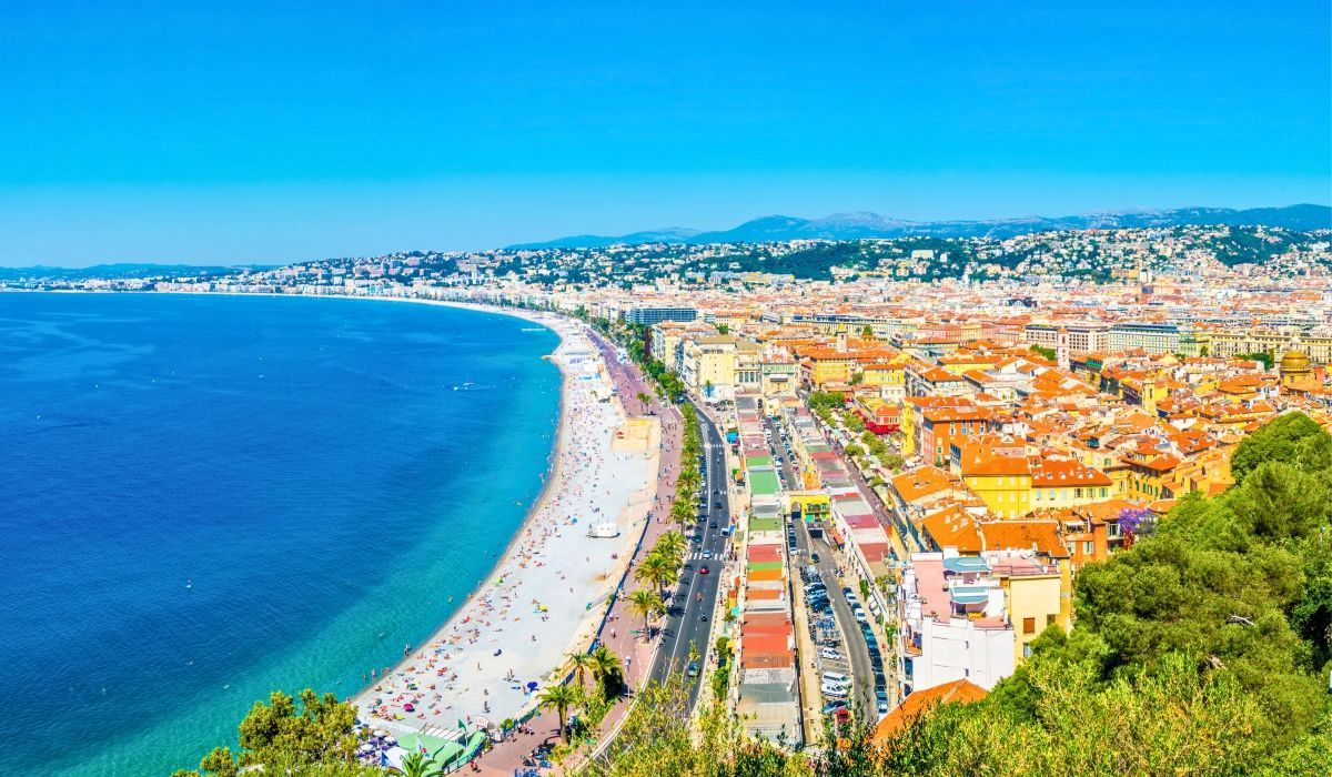 Vibrant aerial view of the Promenade des Anglais and beach in Nice, France, with a sweeping Mediterranean coastline.