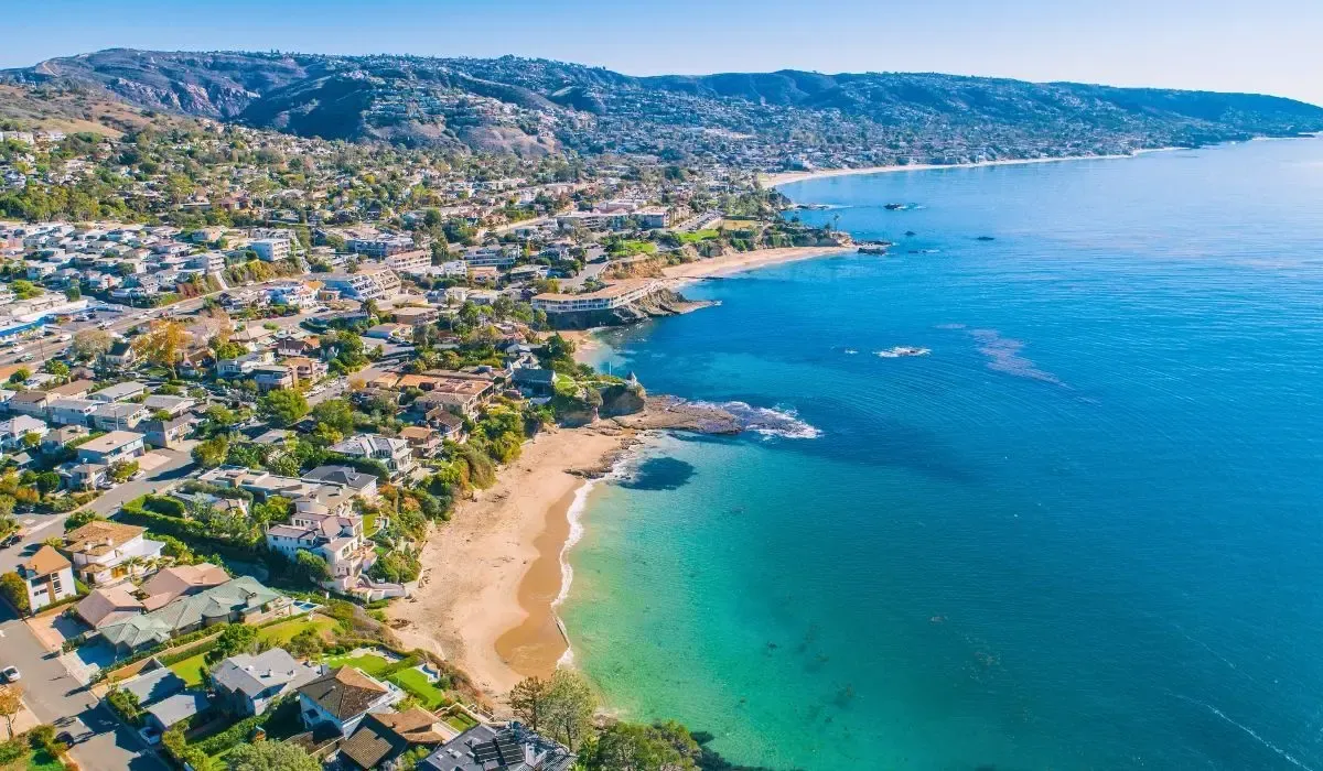 A coastal view of Orange County, displaying beachfront properties, sandy beaches, and the Pacific Ocean under a sunny sky.