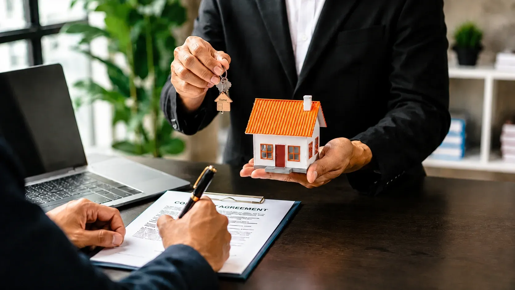 Canadian homebuyer signs mortgage documents while receiving house keys and a model home, symbolizing overseas property ownership.