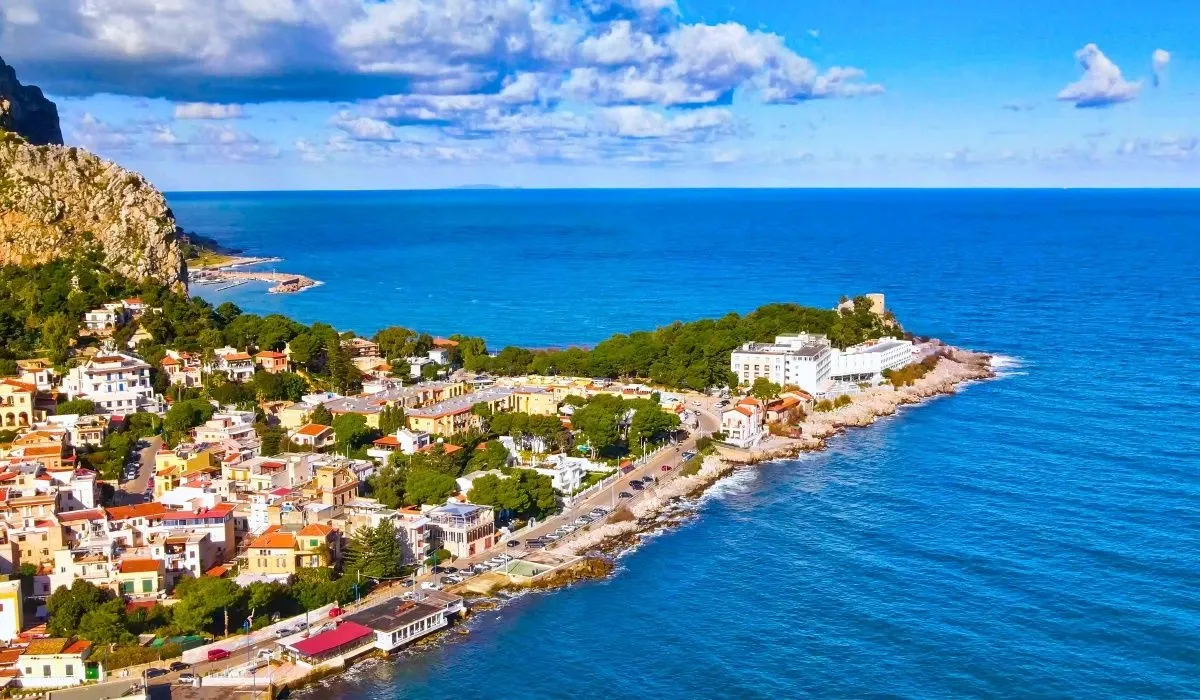 Coastal view of Palermo, Sicily, featuring colorful houses nestled along the Mediterranean shoreline beneath rugged cliffs and blue skies. Canadians considering buying property in Italy can enjoy excellent CAD to EUR rates and low-cost transfers through MTFX.