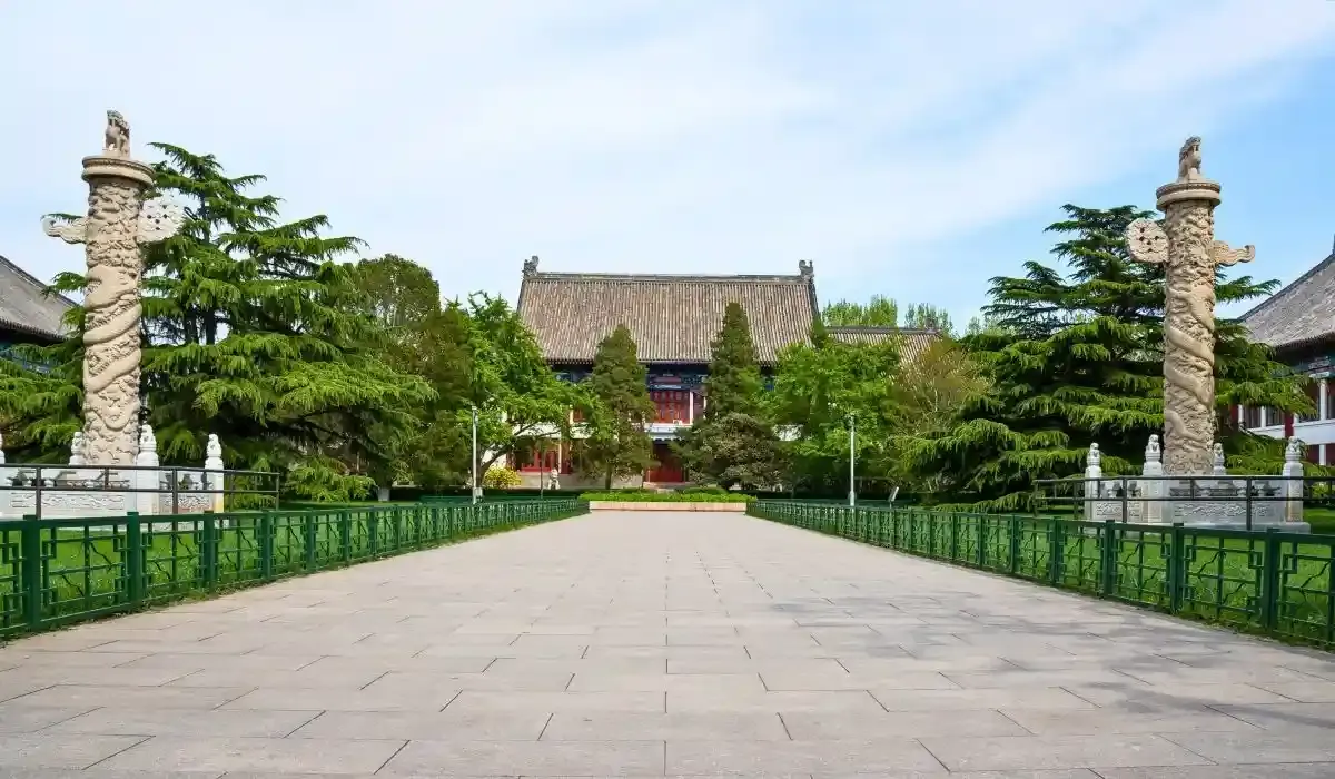 Traditional Chinese architecture at Peking University with a wide stone walkway, flanked by greenery and decorative stone pillars.