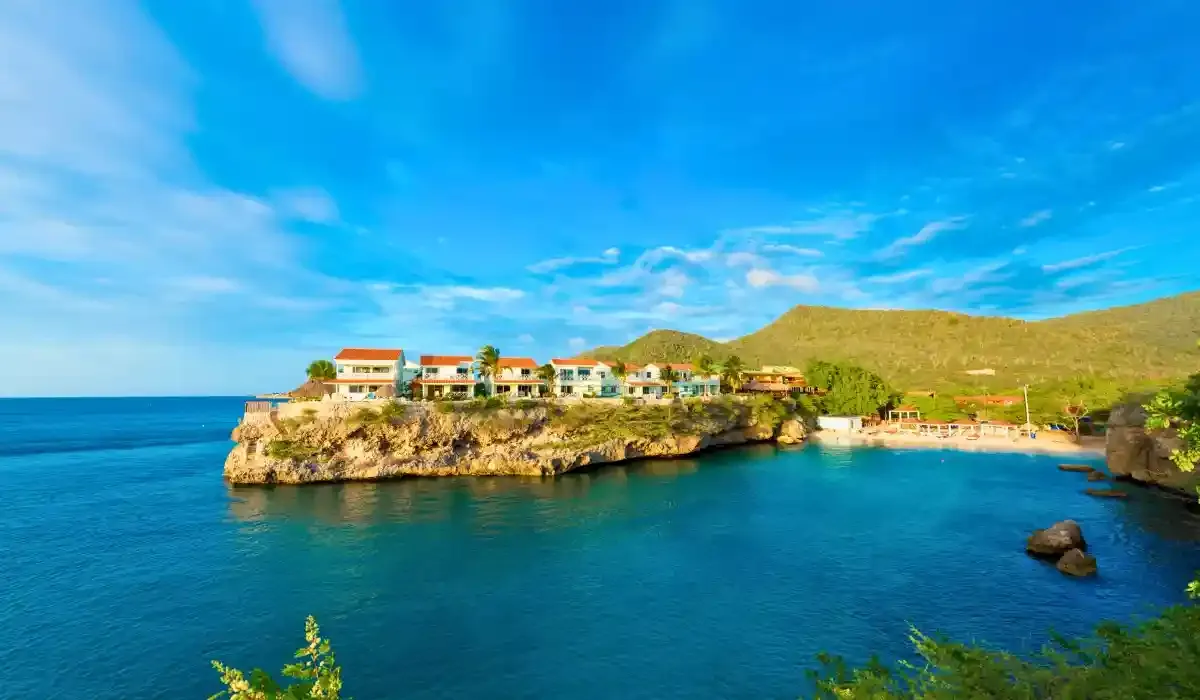 Oceanfront residential villas perched on rocky cliffs in Curacao, overlooking turquoise Caribbean waters under a clear blue sky.