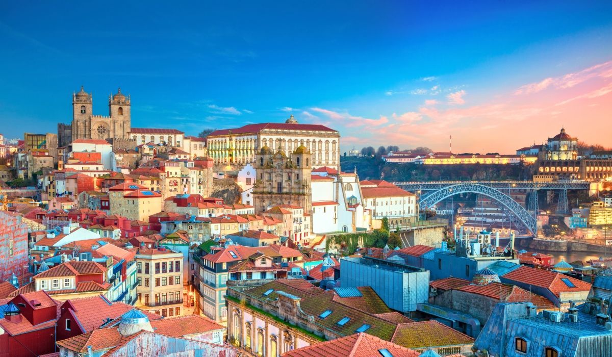 Scenic view of Porto, Portugal at sunset, featuring historic architecture, tiled rooftops, and the Dom Luís I Bridge.