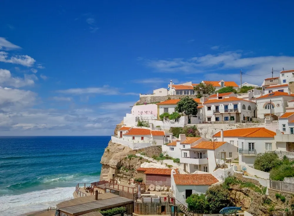 Traditional Portuguese coastal village with whitewashed homes overlooking dramatic cliffs and the Atlantic Ocean.