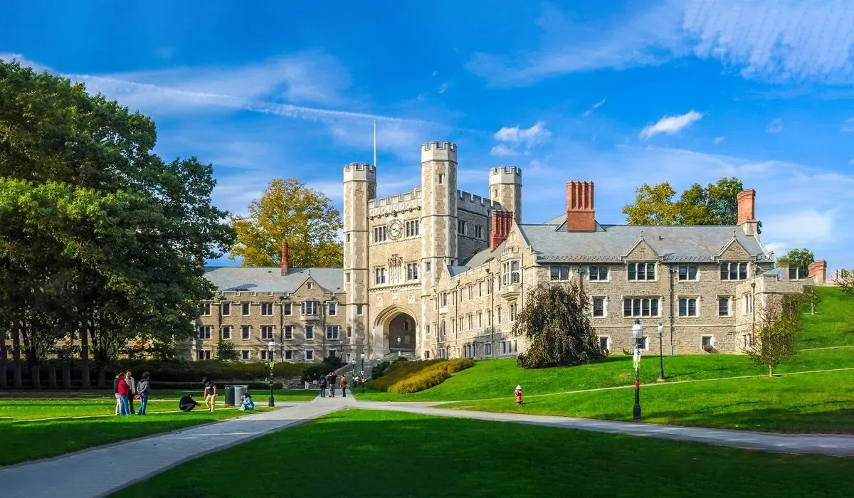 Iconic collegiate Gothic buildings at Princeton University surrounded by manicured lawns and vibrant autumn foliage under a crisp blue sky.