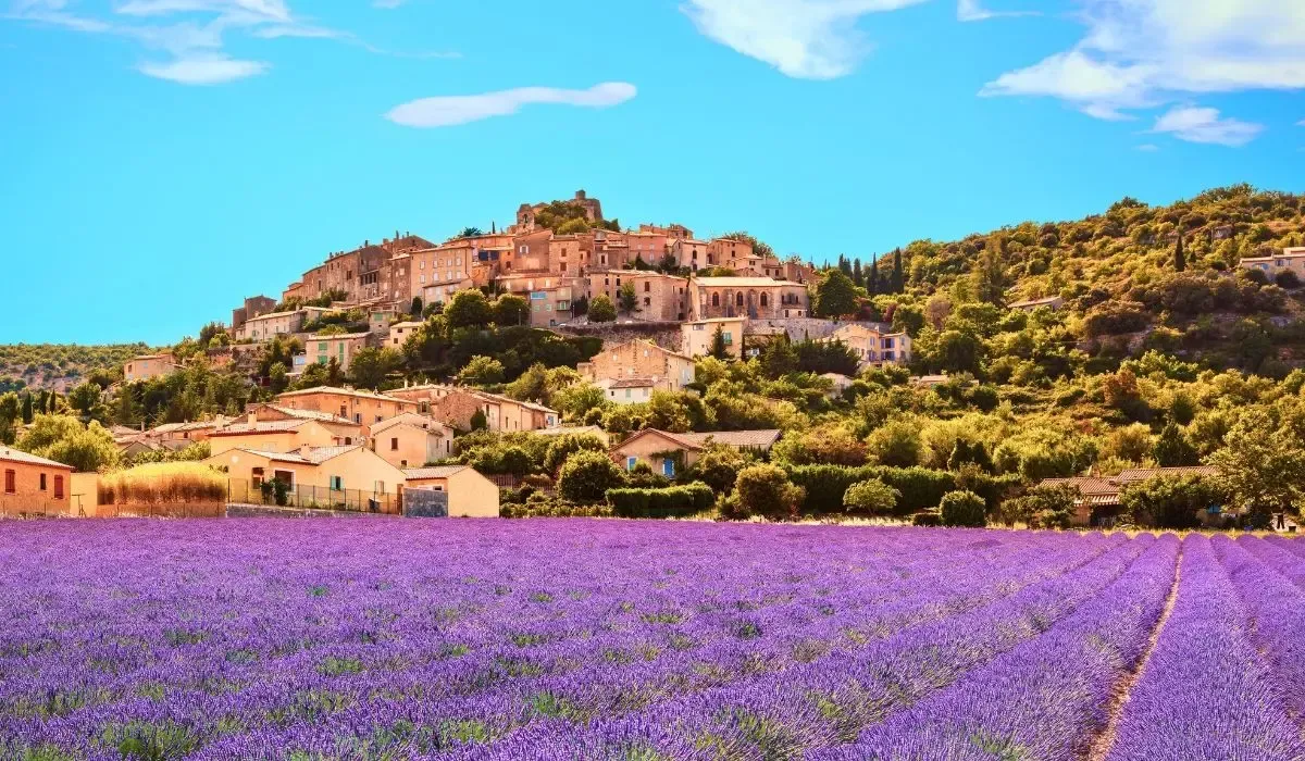 Lavender fields in full bloom leading to a hilltop village in Provence, France under a vivid blue sky. Canadians seeking property in France benefit from competitive CAD to EUR exchange rates and low-cost transfers via MTFX.