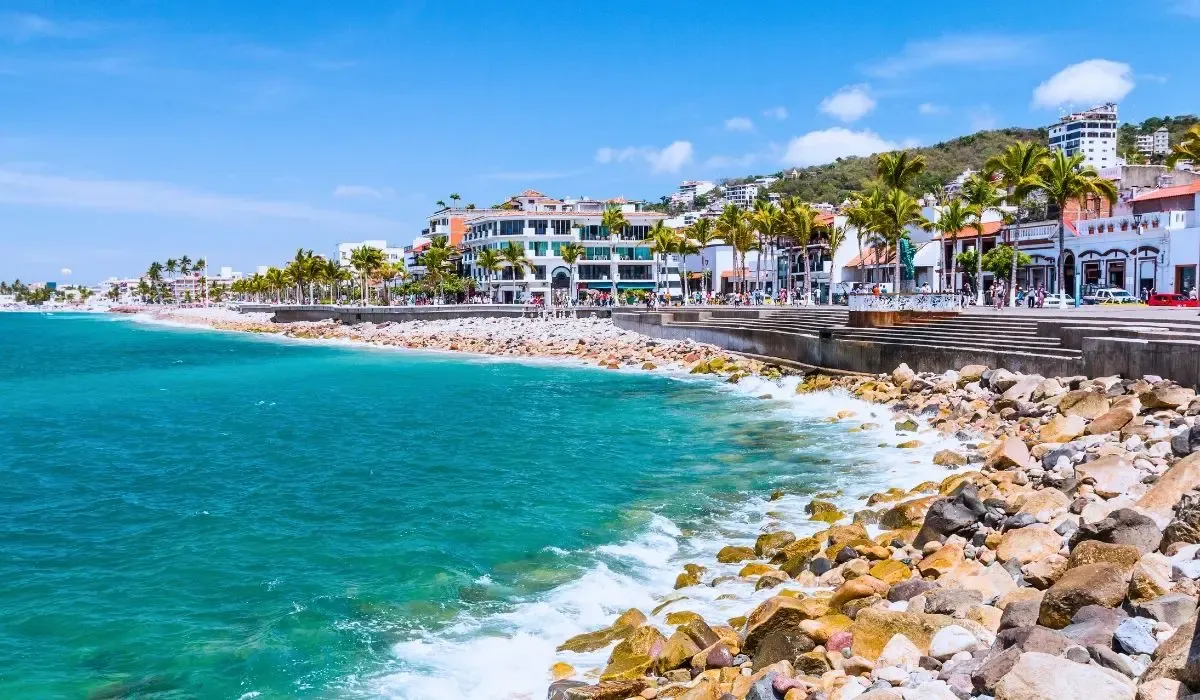 A panoramic view of Puerto Vallarta's coastline, featuring sandy beaches, the Pacific Ocean, and the city's vibrant buildings nestled between lush green hills.