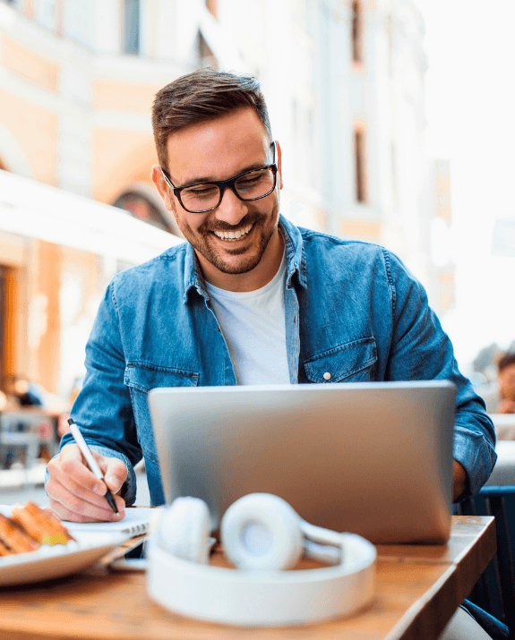Smiling man managing regular international transfers on his laptop at an outdoor café.