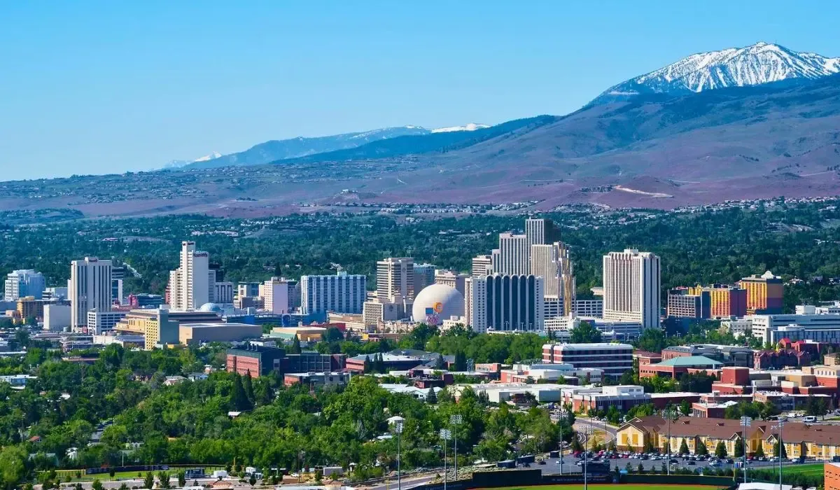 A cityscape of Reno highlighting the downtown area with modern buildings, the Truckee River, and nearby mountainous terrain.